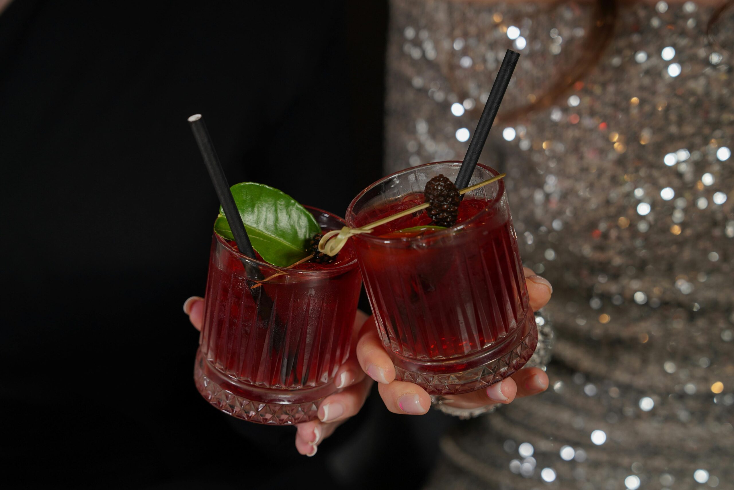 Two rich red cocktails held in hands at an elegant party setting, ideal for lifestyle imagery.